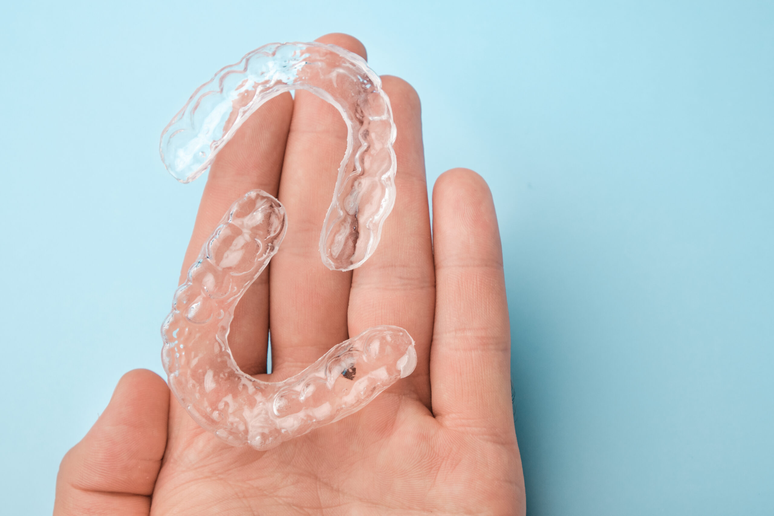 Close-up of a hand holding clear dental aligners on a blue background