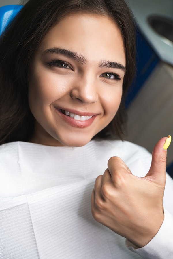happy smiling young woman patient lying on dental chair under the medical lamp in clinic.